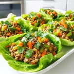 - Ground Chicken: I use 1 pound of ground chicken. It gives a nice texture and flavor. - Sesame Oil: Two tablespoons of sesame oil add a rich, nutty taste. - Fresh Ginger and Garlic: I use 1 tablespoon of minced ginger and 3 cloves of minced garlic. They boost the flavor. - Soy Sauce and Honey: Two tablespoons of soy sauce and 1 tablespoon of honey balance saltiness and sweetness. - Rice Vinegar: I add 1 tablespoon of rice vinegar for a bit of tang. - Vegetables: I include 1 finely grated carrot, 1 diced bell pepper, 3 chopped green onions, and 1/4 cup of chopped water chestnuts. They add crunch and color. - Lettuce Leaves: For wraps, I use leaves from a head of butter or Romaine lettuce. They hold the filling well. - Garnishes: I top my wraps with sesame seeds and fresh cilantro for extra flavor and a pop of color. These ingredients come together to create a fresh and tasty dish. Each part plays a role in making these wraps a delightful experience. - Mince 1 tablespoon of fresh ginger. - Mince 3 cloves of garlic. - Grate 1 carrot finely. - Dice 1 bell pepper. Choose any color you like. - Chop 3 green onions. - Chop 1/4 cup of water chestnuts. - Heat 2 tablespoons of sesame oil in a large skillet over medium heat. - Add the minced ginger and garlic, sautéing them for about 1 minute until they smell great. - Add 1 pound of ground chicken. Break it up with a spatula. Cook until it turns brown, about 5-7 minutes. - Stir in 2 tablespoons of soy sauce, 1 tablespoon of honey, and 1 tablespoon of rice vinegar. Mix well and cook for another 2 minutes. - Add the grated carrot, diced bell pepper, chopped green onions, and chopped water chestnuts. Stir everything together and cook for another 3-4 minutes until the veggies are slightly soft. - Remove the skillet from heat and let the chicken mixture cool a bit. - Spoon the chicken mixture into lettuce leaves to make wraps. - Top each wrap with a sprinkle of sesame seeds and fresh cilantro before serving. - Ensuring the chicken is fully cooked: Cook the ground chicken for 5-7 minutes until it turns brown. Use a spatula to break it apart. Check that no pink remains. This helps ensure safety and flavor in each bite. - Balancing flavor with sauces: Mix soy sauce, honey, and rice vinegar well. This mix gives a sweet and savory taste. Adjust the amount of soy sauce based on your salt preference to get it just right. - Presentation ideas for serving: Lay the lettuce wraps on a colorful platter. You can stack the wraps for a fun look. Add some sesame seeds and cilantro on top for extra flair. - Dipping sauce recommendations: Offer soy sauce on the side for dipping. A spicy chili sauce can add a kick. This lets your guests choose their favorite flavor. - Substituting proteins (e.g., turkey, tofu): You can swap ground chicken for ground turkey or firm tofu. This change can cater to different diets and tastes while keeping the wraps delicious. - Adding different vegetables for variety: Mix in vegetables like cucumber, mushrooms, or bean sprouts. These can add crunch and color to your wraps. Feel free to get creative with what you have on hand! {{image_2}} To store leftovers, place the chicken mixture in an airtight container. Make sure it cools first to keep it fresh. Store it in the refrigerator. Leftovers can stay fresh for about three days. After that, the taste and texture may change. To reheat the chicken mixture, use a skillet over medium heat. Stir often to warm it evenly. You can also use the microwave. Heat in short bursts, stirring in between. This keeps the flavors bright and tasty. Yes, you can freeze the chicken mixture. Use a freezer-safe container or bag. Remove as much air as possible before sealing. This method helps prevent freezer burn. When you’re ready to eat, thaw it overnight in the fridge. Reheat as mentioned above for the best taste. One serving of sesame ginger chicken lettuce wraps has about: - Calories: 250 - Protein: 25 grams - Fats: 12 grams - Carbs: 10 grams These wraps are a great choice for a light meal. They pack a punch with protein while keeping carbs low. Advantages of protein from chicken: Chicken is an excellent protein source. It helps build muscles and keeps you feeling full. The protein also helps your body repair itself after exercise. Benefits of fresh vegetables: Fresh veggies add color and crunch. They are low in calories but high in vitamins. Carrots and bell peppers boost your immune system. Green onions add flavor and support digestion. Water chestnuts give a nice crunch and are low in calories. Making it gluten-free or low-carb: To make this dish gluten-free, use tamari instead of soy sauce. Tamari has a similar taste but is safe for those with gluten issues. For a low-carb option, skip the honey. You can also use a keto-friendly sweetener. This way, you still enjoy the flavors without the carbs. You can use many fun options instead of lettuce. Here are some ideas: - Cabbage leaves: They add a nice crunch. - Collard greens: These are sturdy and hold well. - Nori sheets: Perfect for a sushi twist. - Tortillas: Great for a different flavor. - Pita bread: Soft and tasty for easy wraps. These alternatives can change the flavor and texture. Try them out for a new experience! Yes, you can prepare the filling ahead of time! Here are some tips for meal prepping: - Cook the chicken filling and let it cool. - Store it in an airtight container in the fridge. - You can keep it fresh for up to three days. - When ready, just reheat it before serving. This saves time and makes dinner quick and easy! To complete your meal, consider these side dishes: - Steamed rice: A great base for the wraps. - Quinoa: A healthy grain option. - Asian slaw: Adds crunch and flavor. - Edamame: A protein-packed snack. - Miso soup: A warm, comforting choice. These sides pair well with wraps and round out your meal nicely! This blog post guided you through making delicious sesame ginger chicken lettuce wraps. We explored the needed ingredients, the step-by-step cooking process, and ways to serve these tasty wraps. Remember, cooking is fun and allows you to be creative. Feel free to try different proteins or veggies. Store any leftovers carefully for later use, and don't hesitate to ask if you have more questions. Enjoy your culinary adventure, and savor every bite!